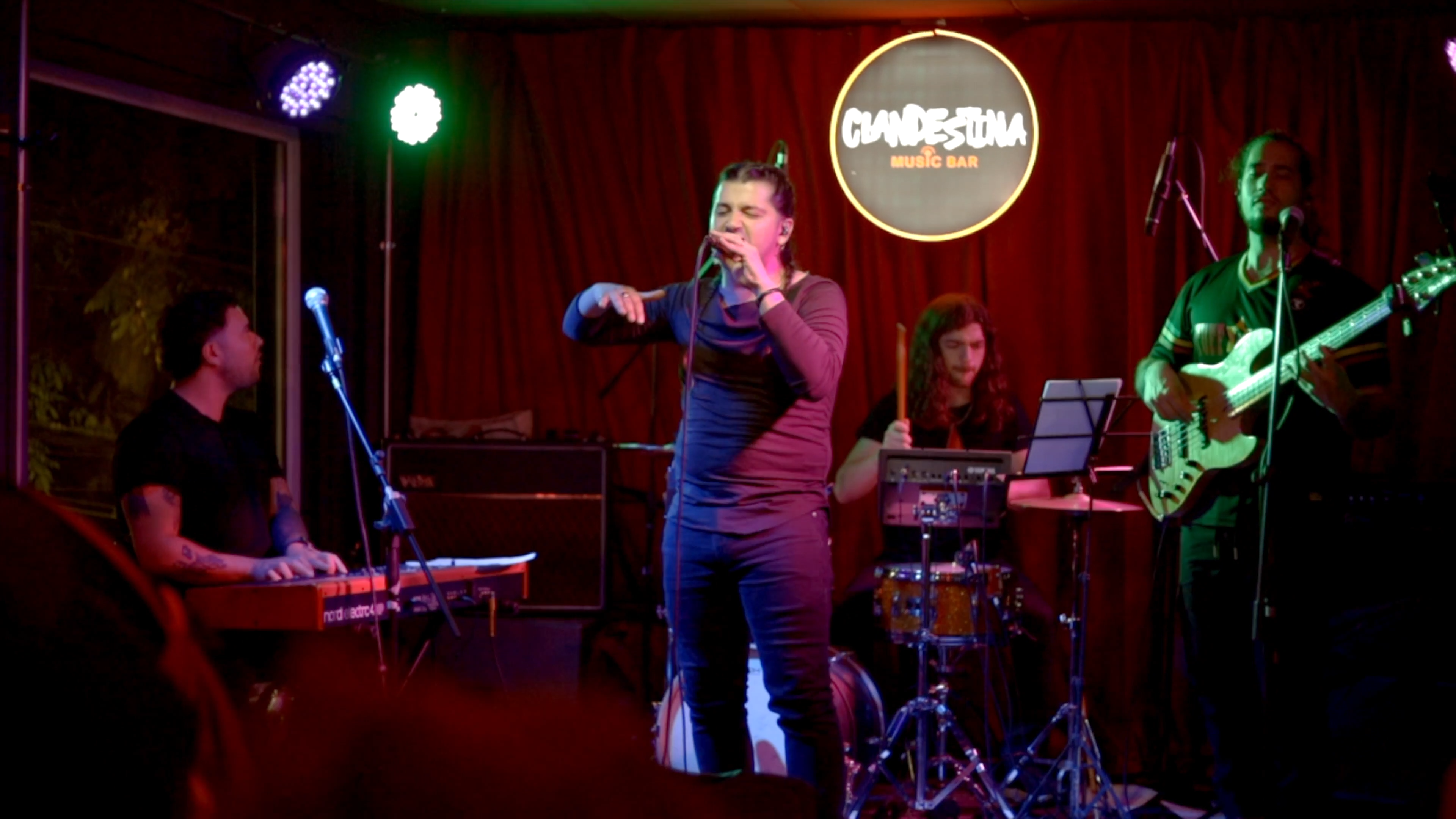 Claude D’Luv cantando con su banda durante la sesión Vigilia en vivo, frente a un telón rojo.