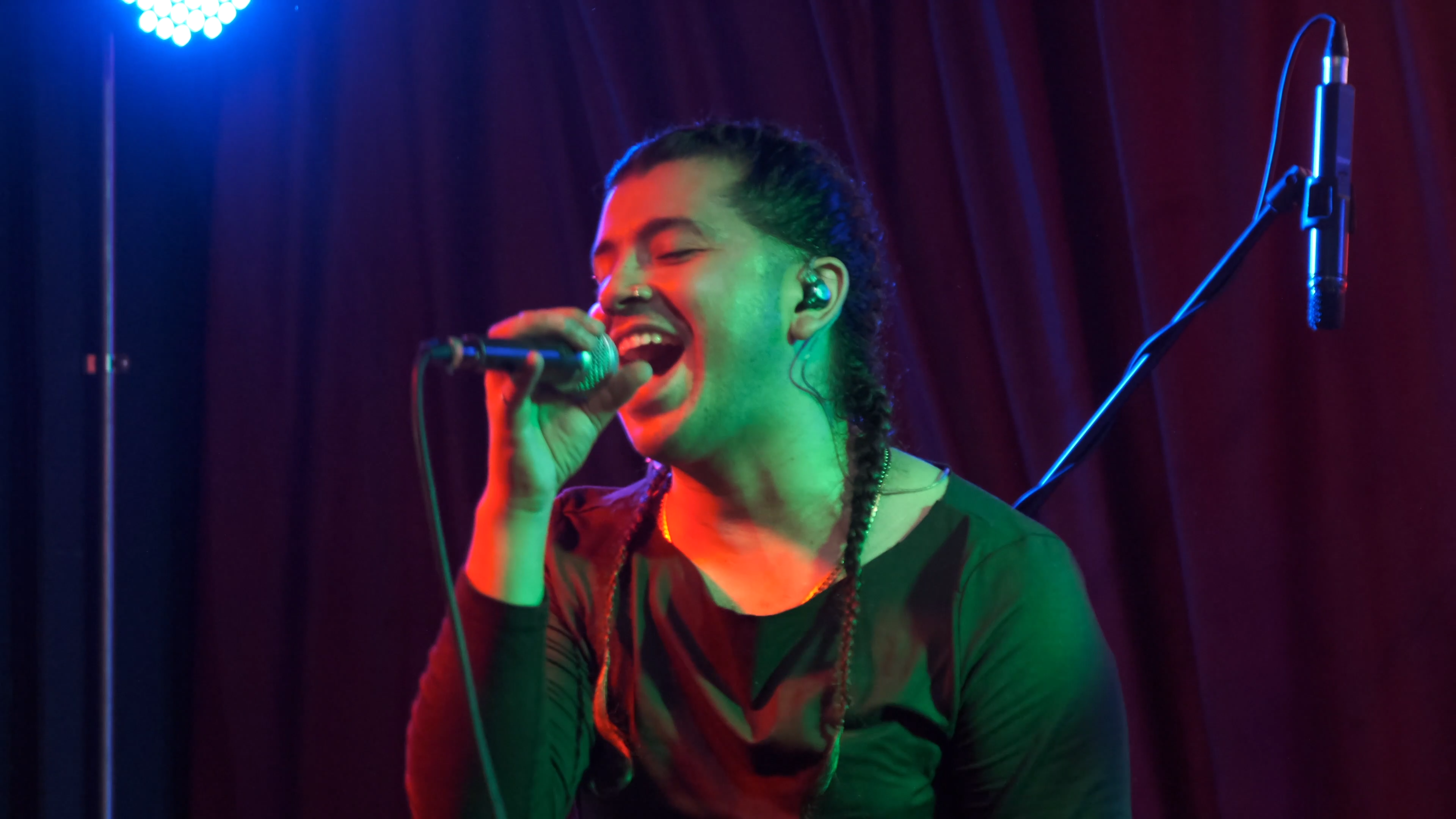 Primer plano de Claude D’Luv cantando al micrófono durante Vigilia en vivo, bajo luces azules y verdes.